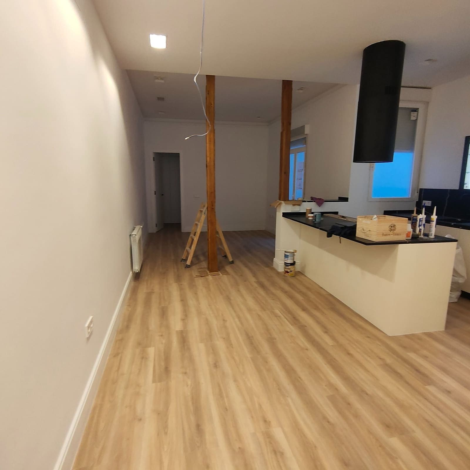 Cocina abierta al salón con la campana cilíndrica negra sobre la isla y suelo laminado
