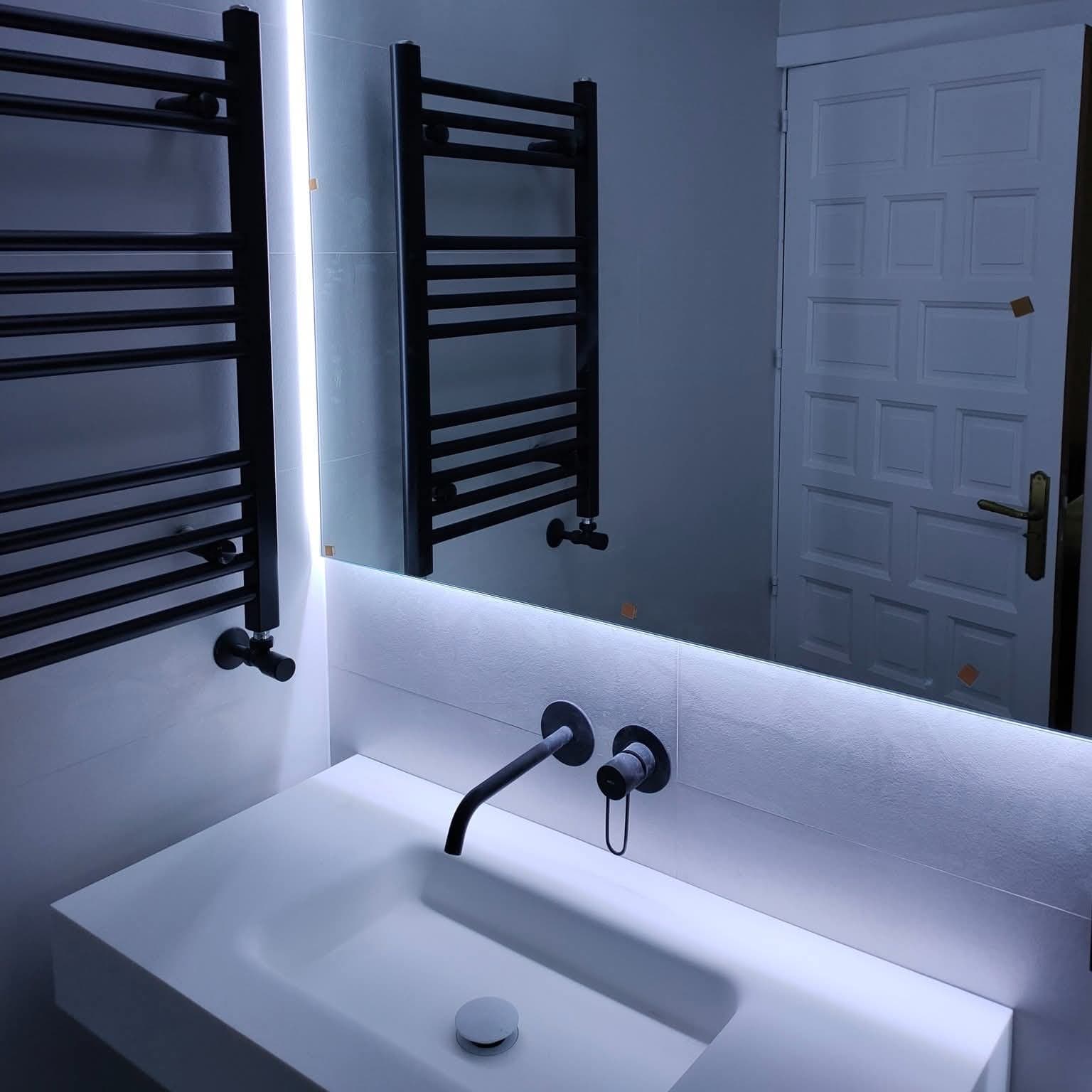 Espejo del baño con iluminación LED en tono cálido y toallero negro