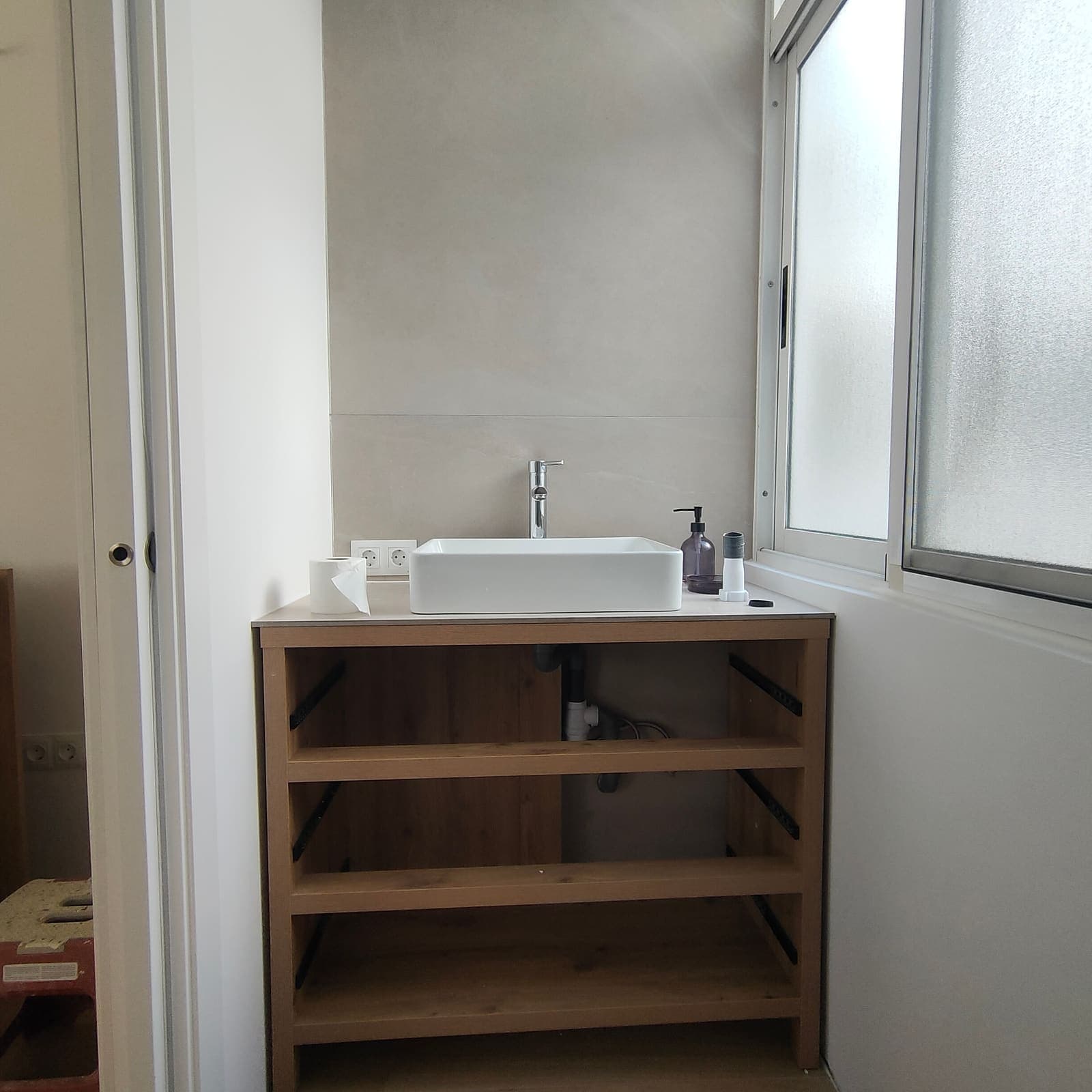 Mueble de lavabo de madera con encimera blanca en el aseo de la vivienda reformada